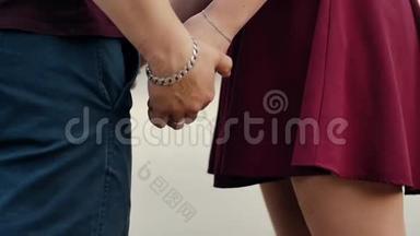 情侣手的特写.. 恋爱中的一对情侣手牵着手站着。 两人都穿着暗红色的衣服。 慢节奏